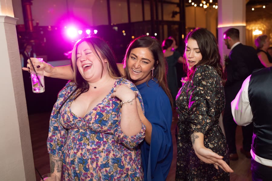 Guests laughing on the dance floor under pink lighting